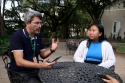 Foto:  Aluna de intercâmbio internacional, Julia Nguyen, sentada numa cadeira nos jardins do INI e conversa com o Prof. Rodrigo Menezes. Ele veste camisa polo preta. Ela veste jaleco branco e uma camisa azul celeste por baixo do jaleco.