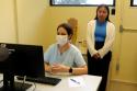 Foto: Aluna de intercâmbio internacional, Julia Nguyen, observa medica usando o computador dentro do ambulatório de dermatologia do INI/Fiocruz. 