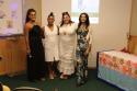 Foto com quatro mulheres trans, durante o evento no INI de celebração do Dia Nacional de Visibilidade Trans. A primeira mede cerca de 1,75; vestido preto, cabelos castanhos, compridos abaixo dos ombros, a segunda tem 172 cm, veste um vestido branco e tem cabelos pretos e presos por um coque no alto da cabeça; a terceira, tem cerca de 176 cm, tem cabelos castanho-escuro, na altura dos ombros, ela veste um vestido longo branco; a quarta mulher tem 172 cm, tem cabelos negros na altura do ombros, veste macacão 