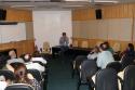 Foto do Auditório do INI com o Dr. Estevão Portela na frente apoiado na mesa discursando.